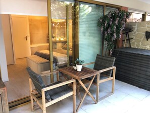 Ein gemütlicher Patio-Bereich mit einem Holztisch und zwei Stühlen, einem Steinkamin und Blick durch eine Glastür in ein Schlafzimmer.