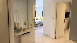 Habitación de hotel moderna con un espejo grande, una tocador con frascos de vidrio y una cama con una decoración en tonos blanco y amarillo.