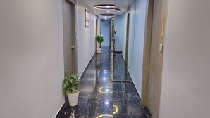 Um corredor com piso de mármore, plantas em vasos e uma porta com o número.
