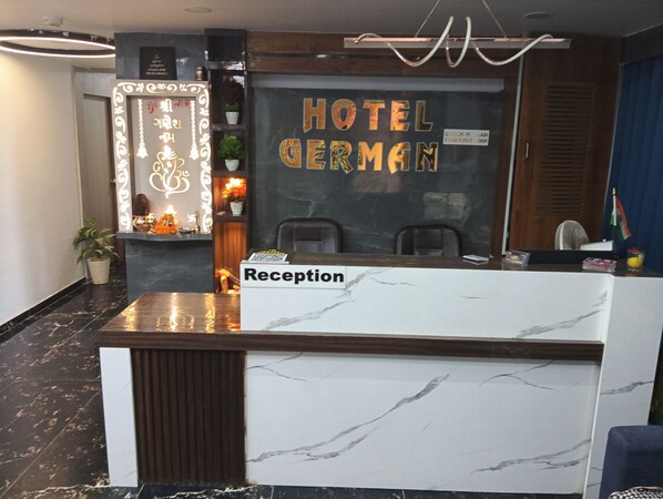 A szálloda recepciós területe márvány pulttal, egy „Recepció” felirattal ellátott recepciós asztallal és egy „HOTEL GERMAN” feliratú táblával.