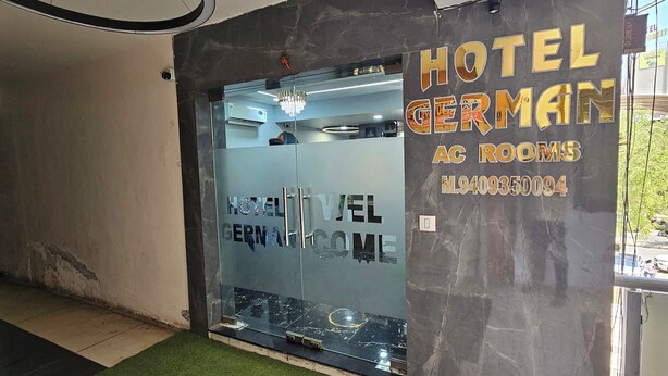 Entrada de hotel com porta de vidro, um lustre e uma placa indicando 'Hotel Germain AC Rooms'.