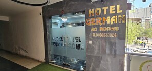 A hotel entrance with a glass door, a chandelier, and a sign indicating 'Hotel Germain AC Rooms.' - HOTEL GERMAN (Gandhinagar)