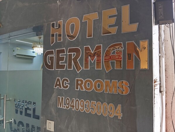 A wall with the text "HOTEL GERMAN AC ROOMS" and a phone number. - HOTEL GERMAN (Gandhinagar)