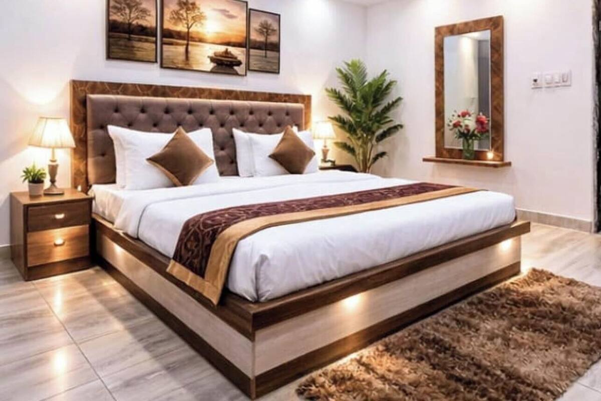 Un dormitorio con una cama grande, una mesita de noche, una lámpara, un espejo y una planta.