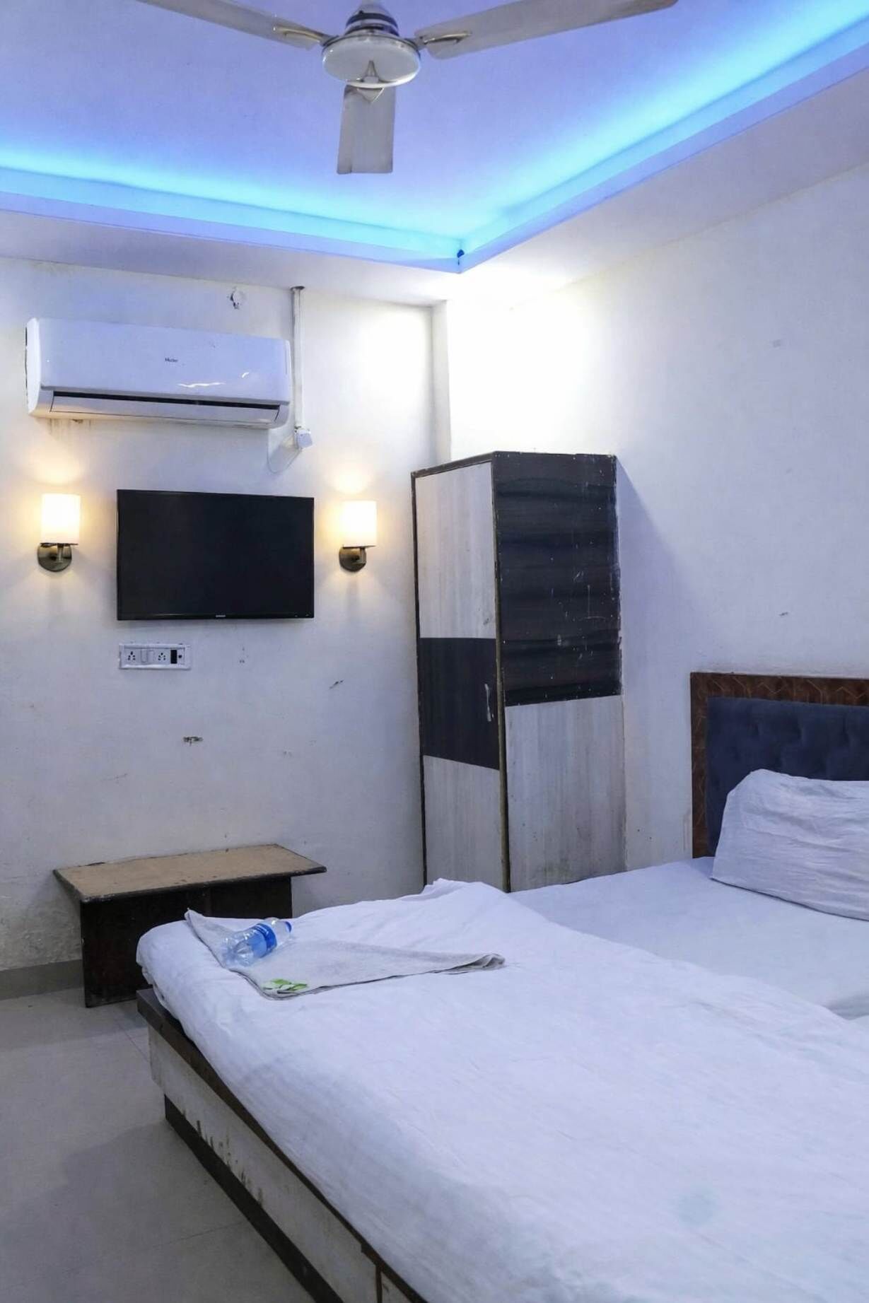 Una habitación de hotel con cama, mesita de noche, televisor montado en la pared y aire acondicionado.