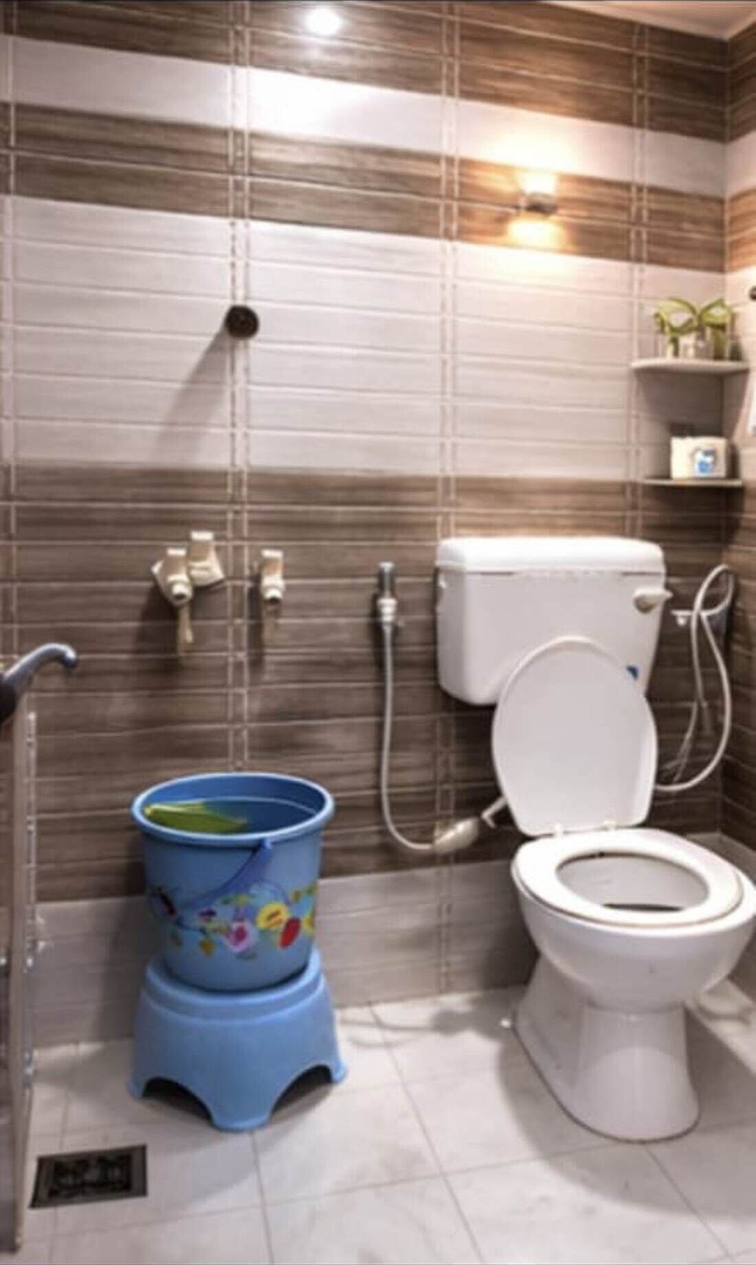A bathroom with a toilet, a blue bucket, and a shower.