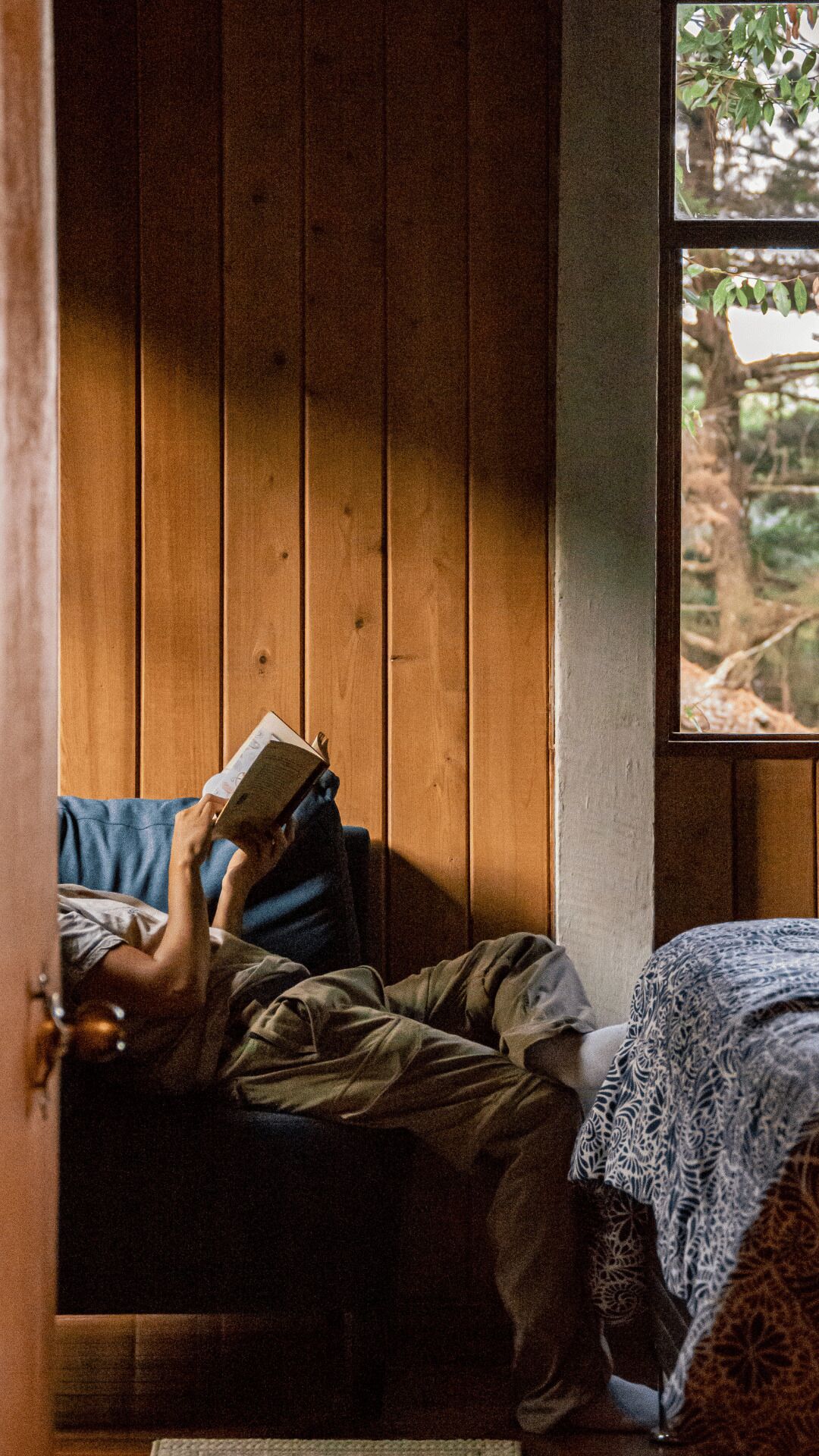 A person lying on a bed in a room with wooden walls and a window.