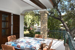 An outdoor patio with a table set for two, surrounded by wooden chairs, a stone pillar, and a green metal railing. - Apartmento a 3-minute walk from the beach. (Santa Maria Navarrese)