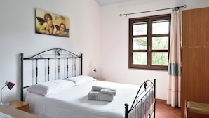 A bedroom with a bed, a desk, a chair, a window with curtains, and a painting on the wall.