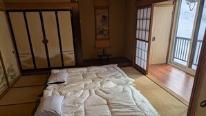 Et traditionelt japansk værelse med tatamimåtter, en stor seng med hvide sengetøj, skydedøre og udsigt til et snæret landskab.