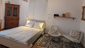 Quarto com uma cama, um armário de madeira, uma cadeira e uma estante com livros.