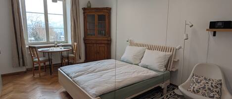 Un dormitorio con cama, silla, mesa y ventana.