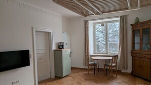 Quarto com piso de madeira em padrão herringbone, televisão na parede, armário com cafeteira, janela com cortinas e armário de madeira com portas de vidro.