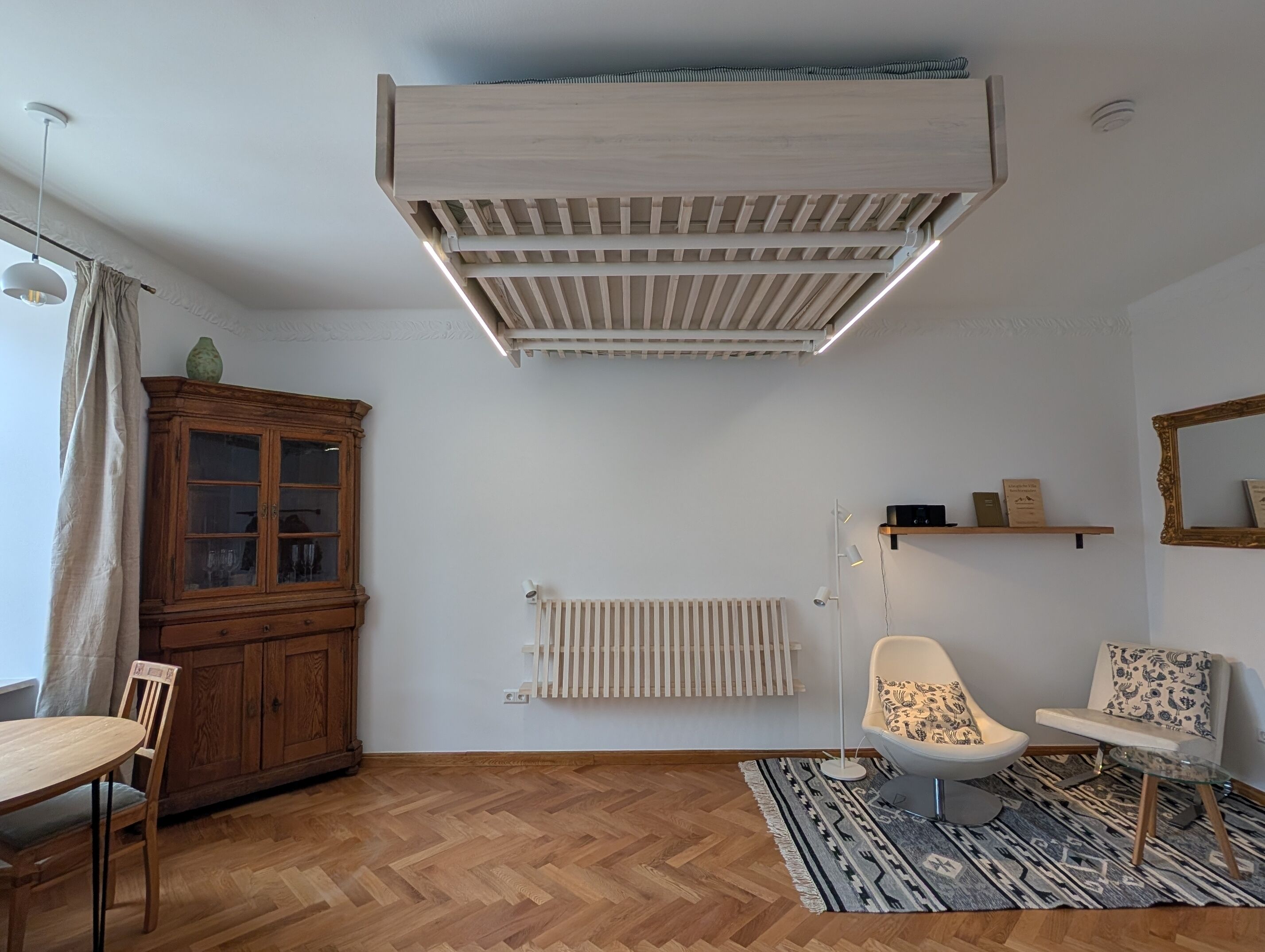 Una sala de estar moderna con un mueble de madera, un radiador, una silla, una mesita y un lámpara colgante.