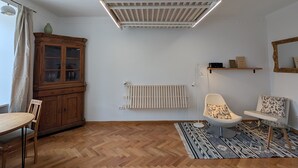Uma sala de estar moderna com um armário de madeira, um radiador, uma cadeira, uma mesinha e um lustre.