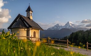 Une petite église dotée d’un clocher, entourée d’une végétation luxuriante et avec une chaîne de montagnes en toile de fond.