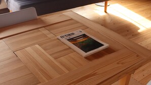 A wooden dining table with a book, a white chair, and a dark sofa in the background.