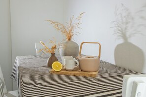 Ein Tisch mit einer gestreiften Tischdecke, einer Vase mit Trockenpflanzen, einer Tasse, einem Teekessel und einem Zitronenscheibchen.