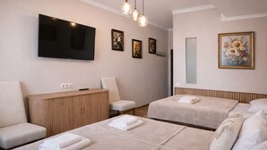 Hotellihuone, jossa on kaksi sänkyä, televisio, puinen kaappi ja tuoli.