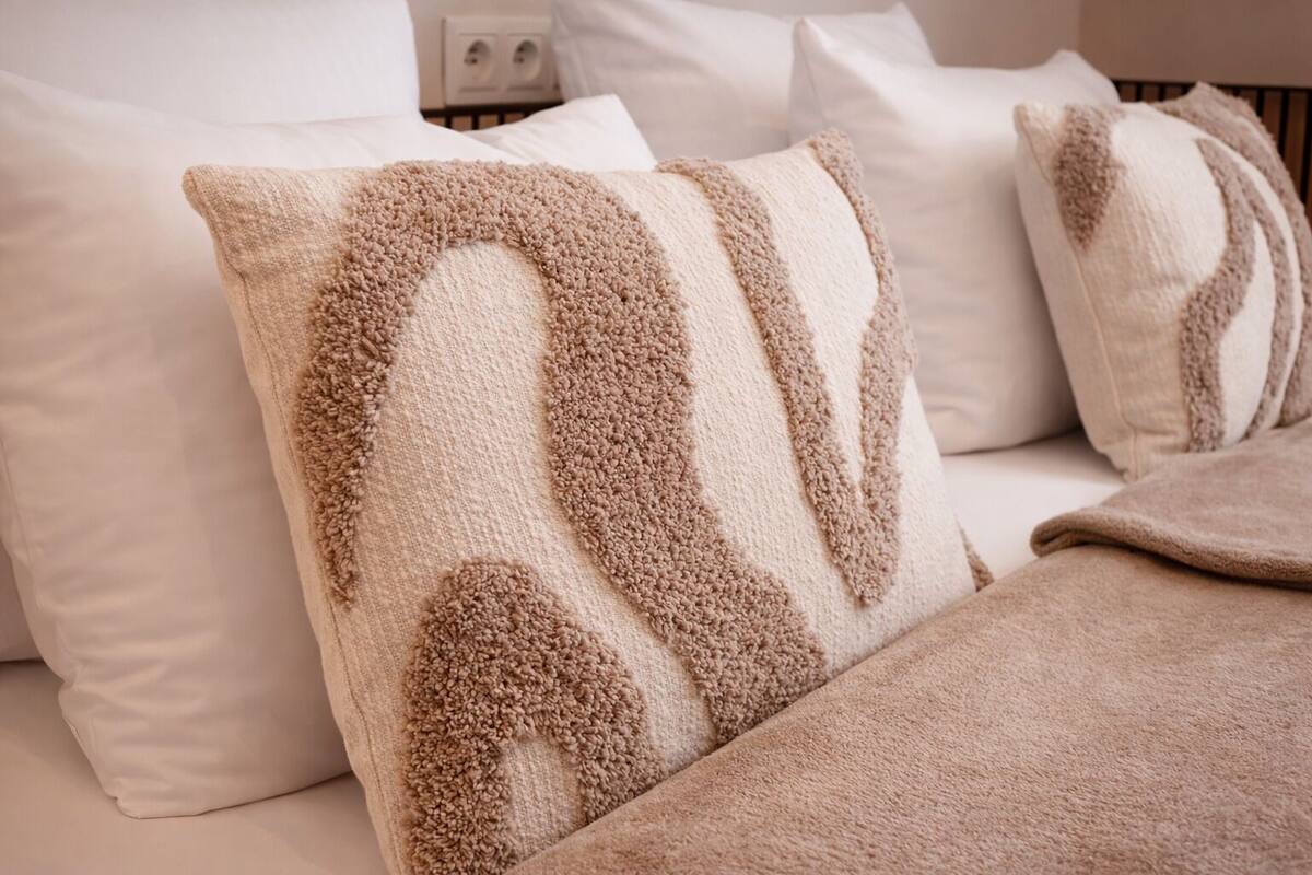 Un lit avec des oreillers blancs et une couverture beige.