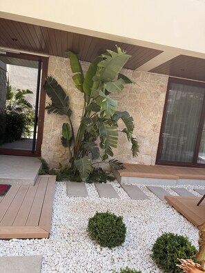 A modern outdoor area with a stone wall, a large plant, a wooden deck, and a small garden with white pebbles. - ARKK ROOMS (Antalya)