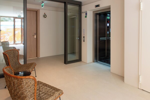 A hotel lobby with wicker chairs, a glass door, and an elevator. - ARKK ROOMS (Antalya)
