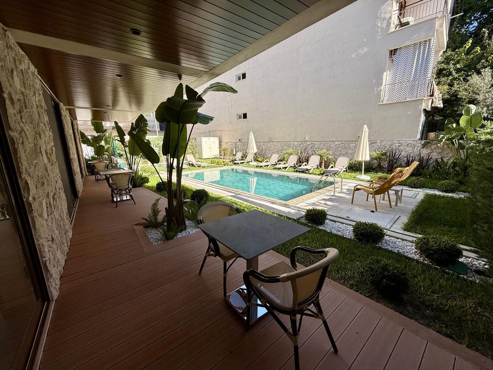 Eine Holzterrasse mit Tisch, Stühlen, einem Pool und Liegestühlen.