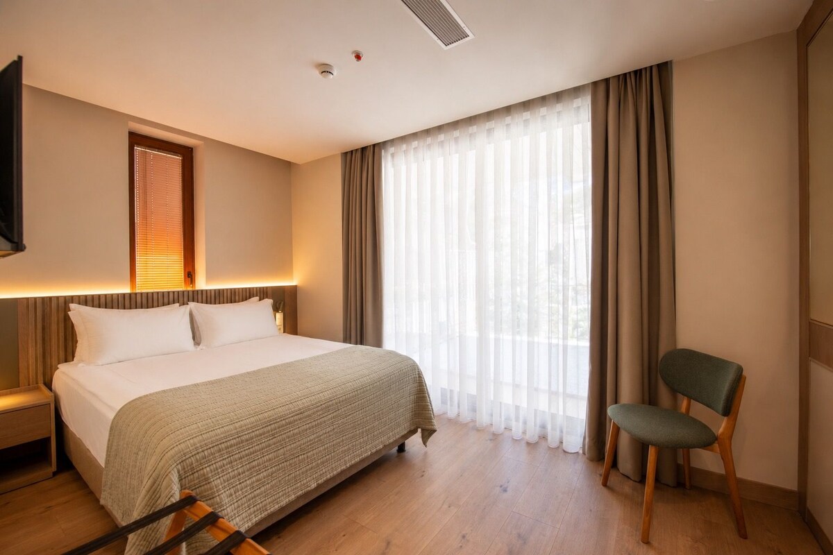 A hotel room with a bed, a chair, a TV, and a window with curtains.