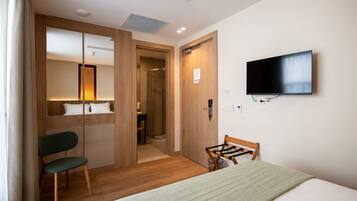 Une chambre d’hôtel équipée d’un lit, d’une télévision, d’une armoire en bois, d’un miroir et d’une douche.
