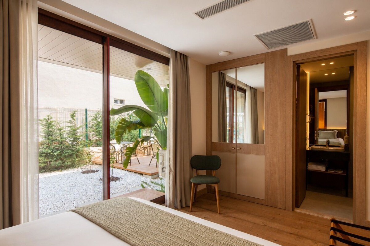 A hotel room with a bed, a chair, a large mirror, and a view of the outside.