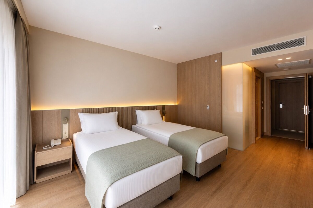 Una camera d'albergo con due letti, un comodino con il telefono, una lampada a parete e una porta che dà su un'altra stanza.