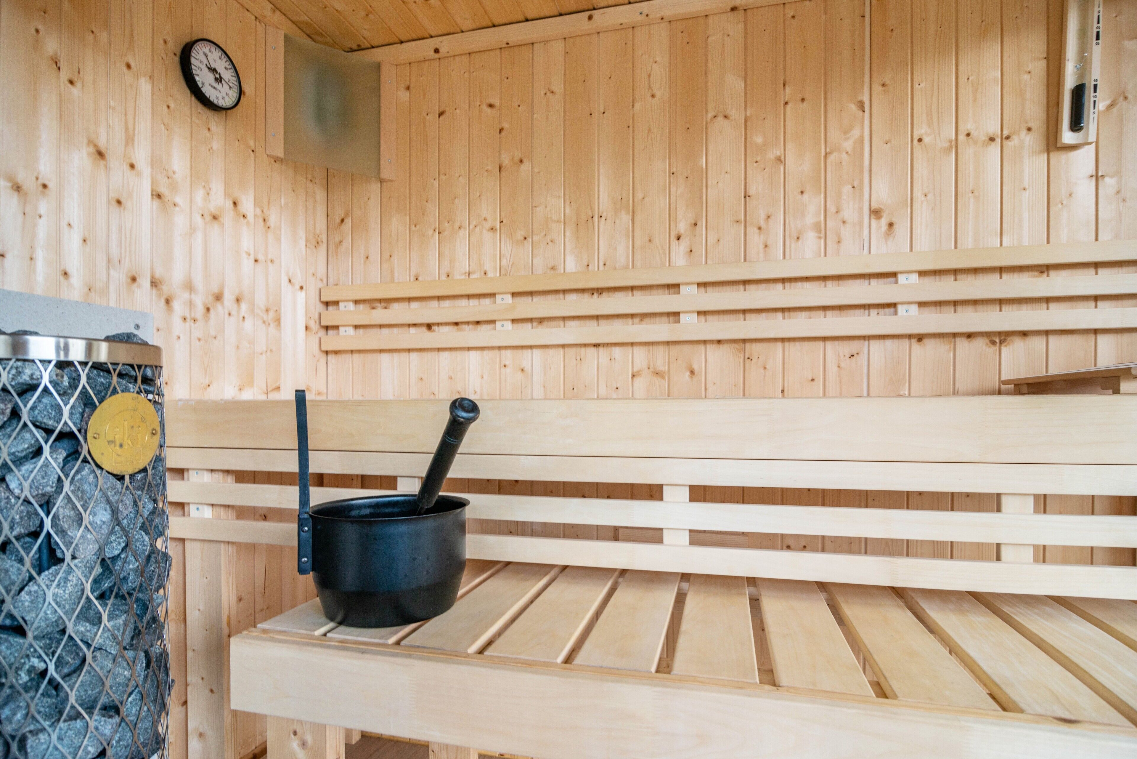 A wooden sauna bench with a black pot and a ladle on it.