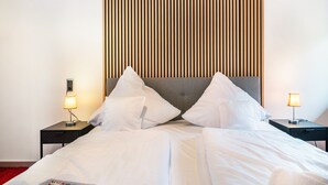 Un letto rifatto con lenzuola bianche, due comodini con lampade e un pannello di legno verticale sulla parete.