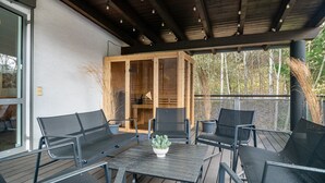 Patio esterno con pavimento in legno, un tavolo con sedie e un armadietto in legno con vetrate.