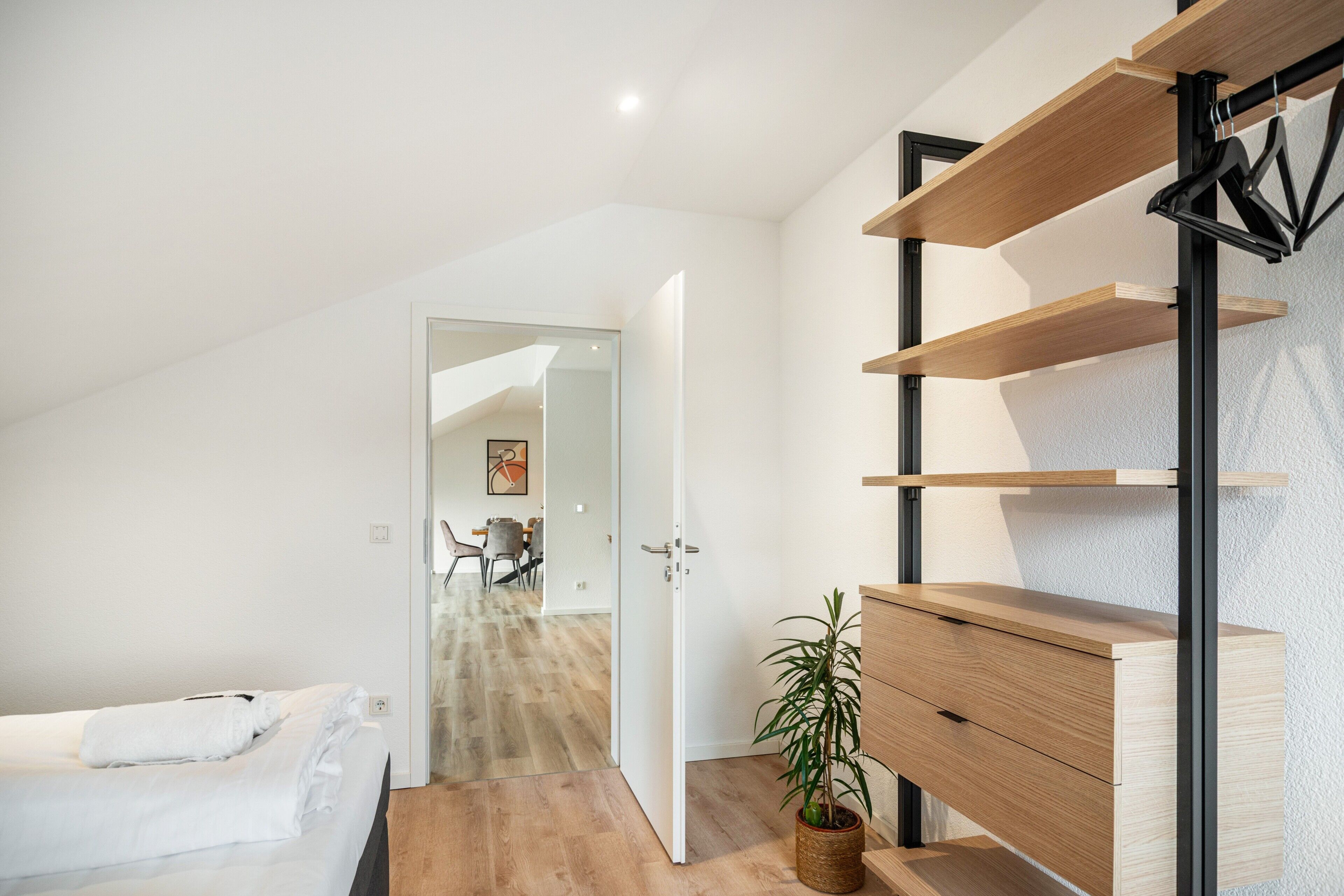 Ein modernes Schlafzimmer mit Bett, einem Holzkasten, einer Topfpflanze und einer eingebauten Schrankwand.