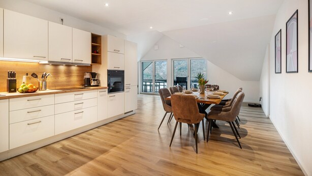 A modern kitchen with white cabinets, a dining area with a wooden table and chairs, and large windows. - Apartment 'Moselbude Kröv' with Moselle View, Sauna, Terrace, E-Bikes Included, Grill (Kröv)