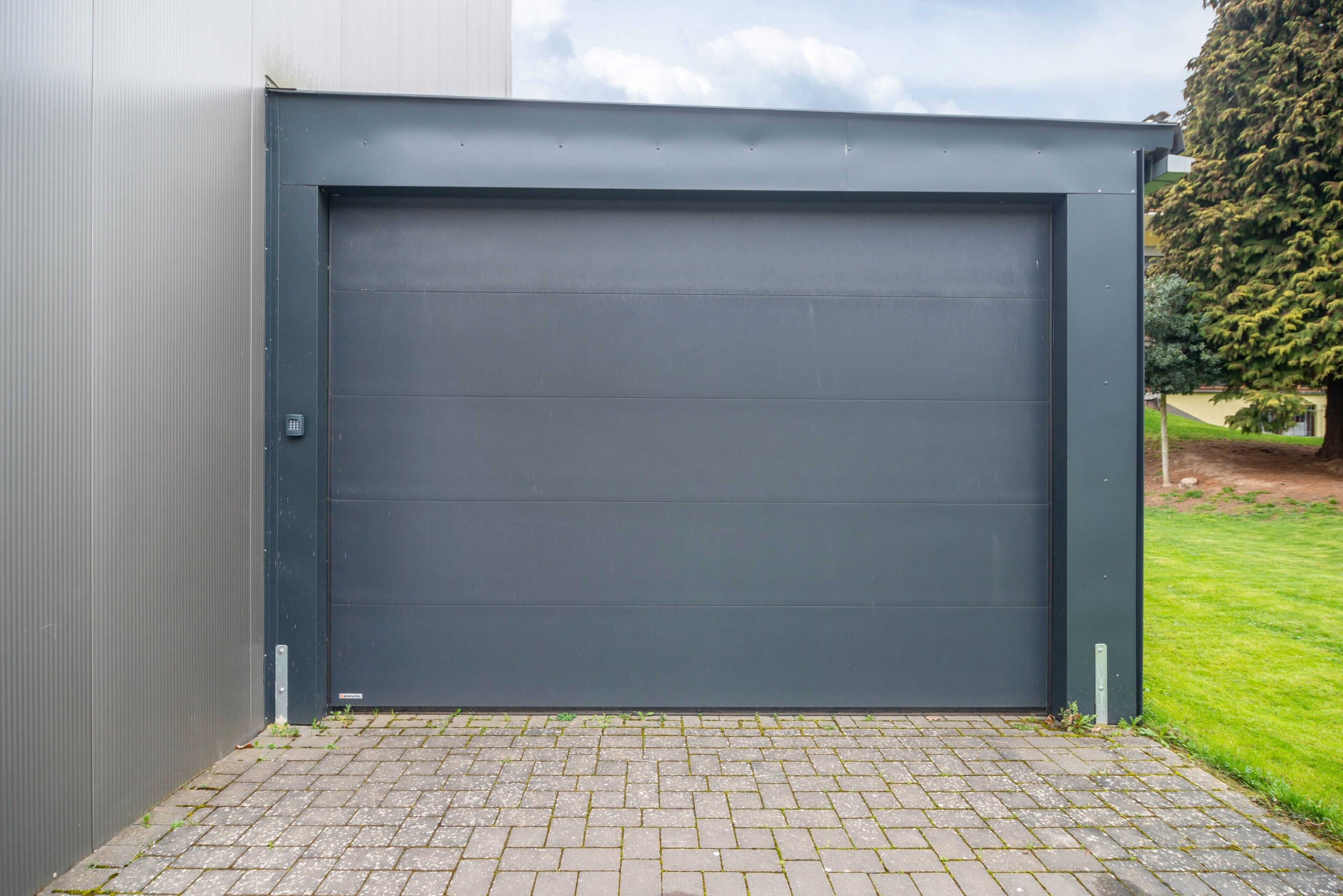 Geschlossene graue Garagentür mit Metallwand und befestigter Auffahrt.