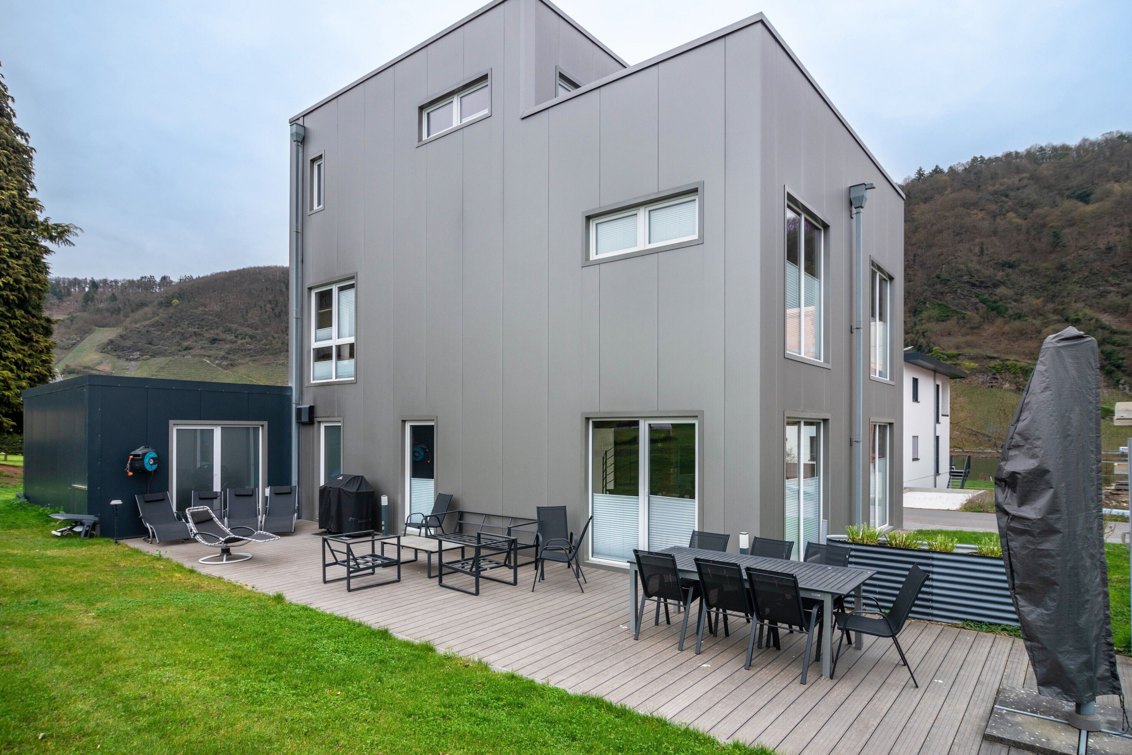 A modern two-story building with a deck, outdoor seating, and a barbecue area.