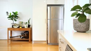 Una cocina moderna con un refrigerador de acero inoxidable, una mesa de madera con plantas y una guitarra.
