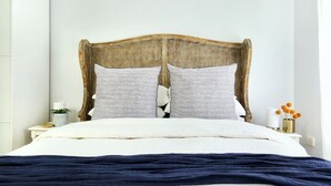 Una cama con cabecera de mimbre, dos almohadas, una colcha blanca y una manta azul oscuro.
