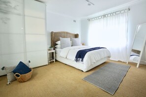 A bedroom with a bed, a bedside table, a hanging chair, a wardrobe, and a window with curtains. - Coastal Stay | 500m to Beach & Cronulla Centre (Cronulla)