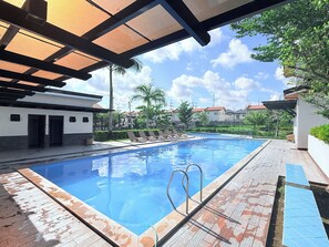 A swimming pool with a sunshade structure, lounge chairs, and a clear sky.