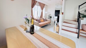 A modern living room with a sofa, a dining table with a vase of flowers, a clock on the wall, and a staircase leading to another level.