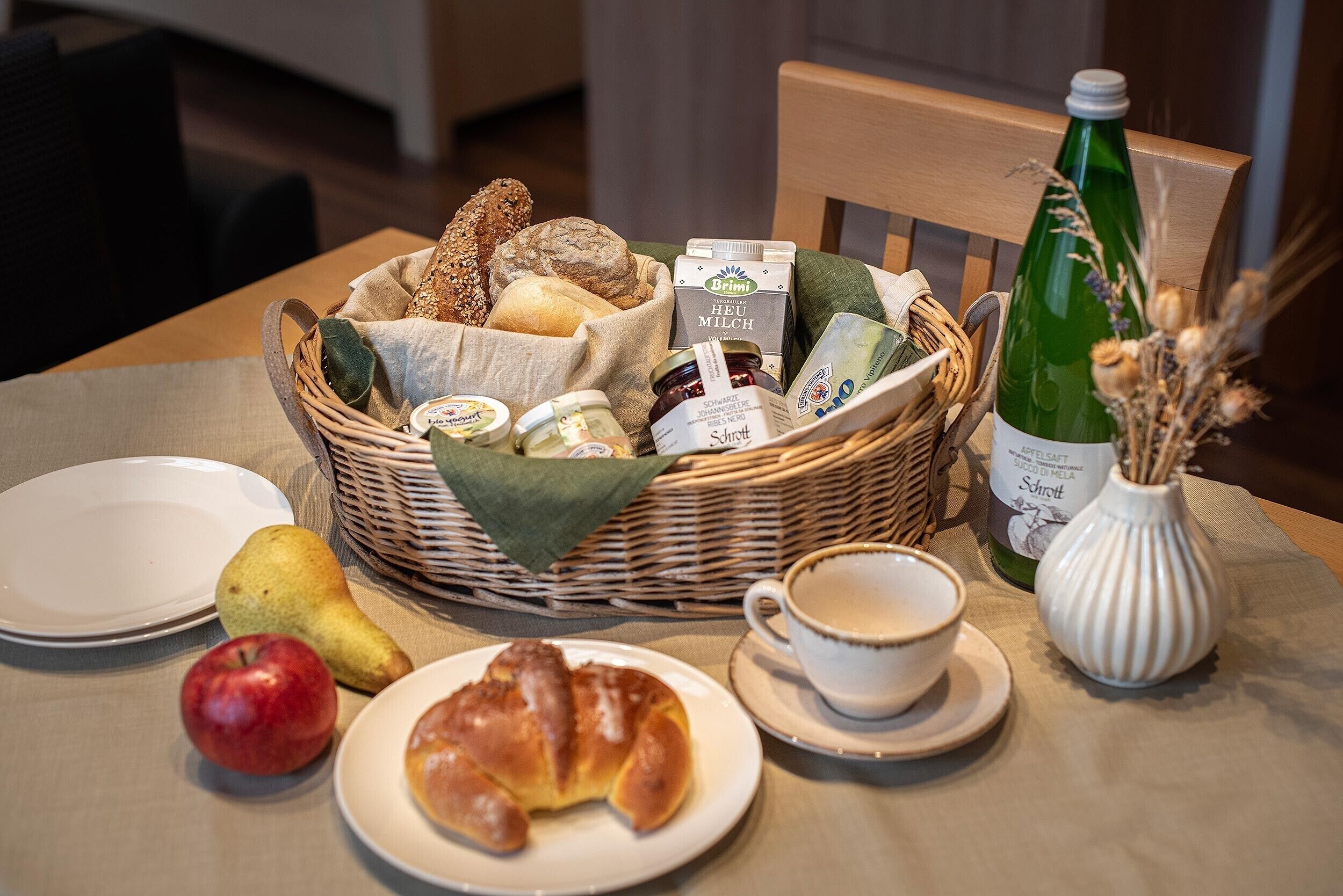 Una colazione con pane, formaggio, una bottiglia, un croissant, una mela e una tazza.