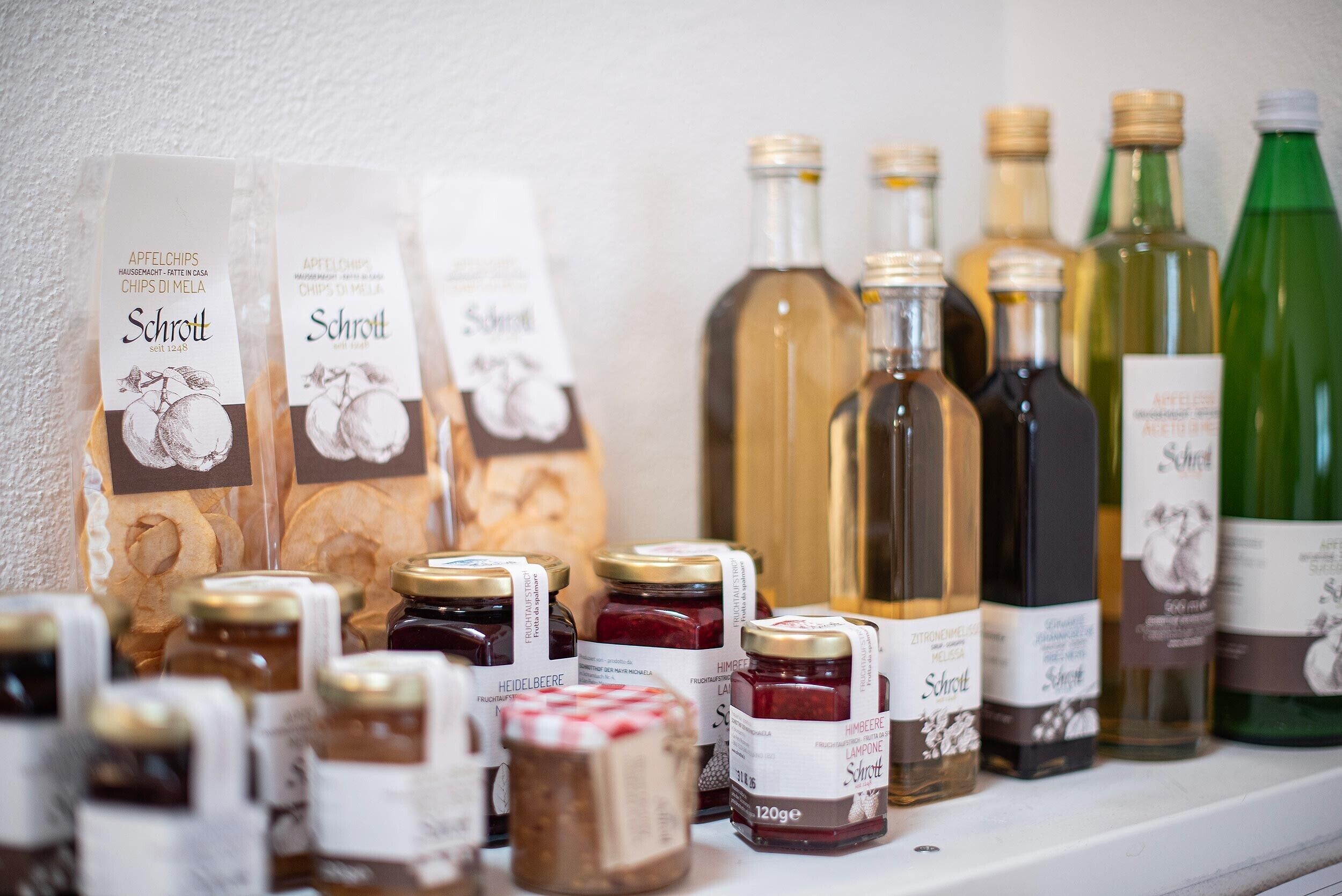 On peut voir une variété de produits alimentaires sur une étagère, notamment des pots de confiture et des bouteilles d’huile d’olive.