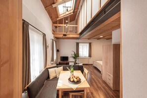 Un interior moderno con zona de comedor, sofá, televisor y vigas de madera.