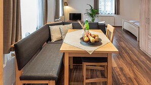 Tilava huone, jossa on korkea katto, puiset kattopalkit, ruokapöytä ja penkki sekä suuri ikkuna.