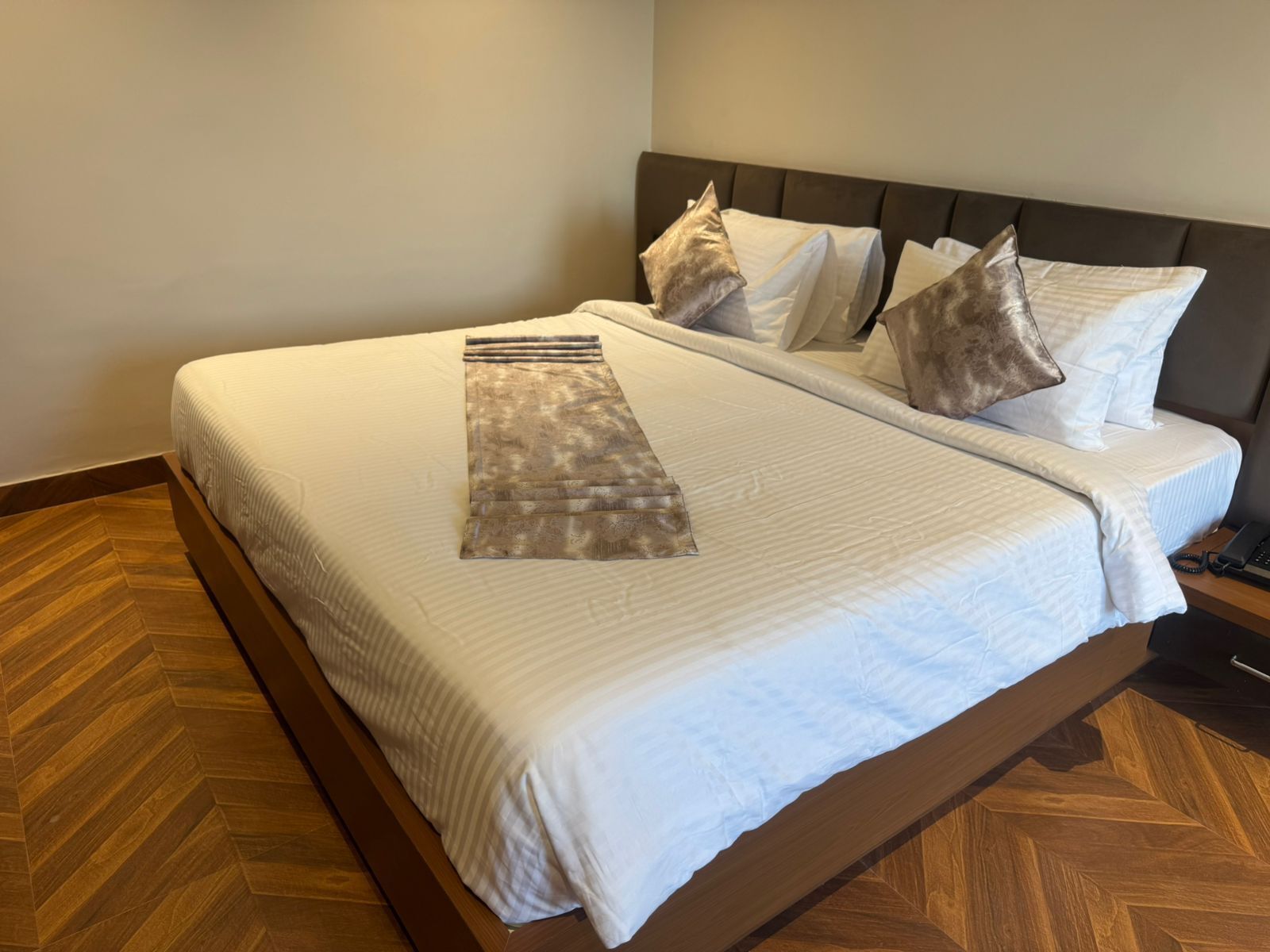A neatly made bed with a patterned runner, a wooden floor, and a headboard with multiple pillows.