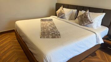 A neatly made bed with a patterned runner, a wooden floor, and a headboard with multiple pillows.