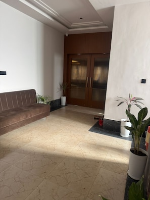 A lobby with a brown sofa, potted plants, a tiled floor, and a wooden door with glass panels. - Hotel Golden Bird (Dabok)